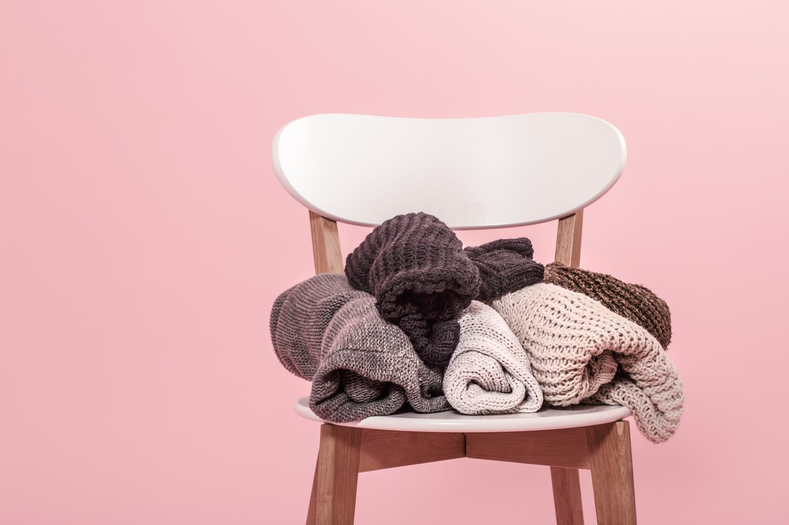 Gestapelte Strickpullover auf weissem Stuhl